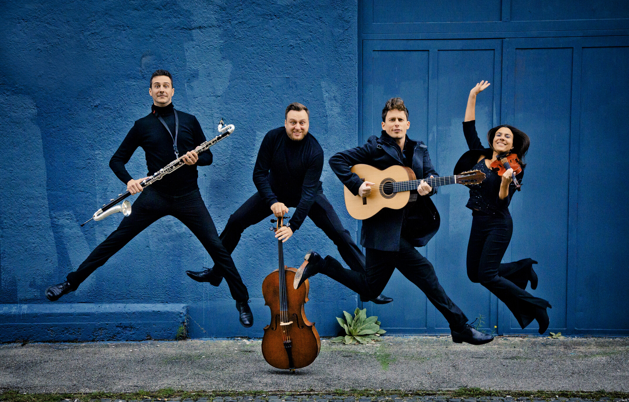 das vierköpfige Ensemble Passo Avanti springt mit seinen Instrumenten vor einer blauen Hauswand in die Höhe
