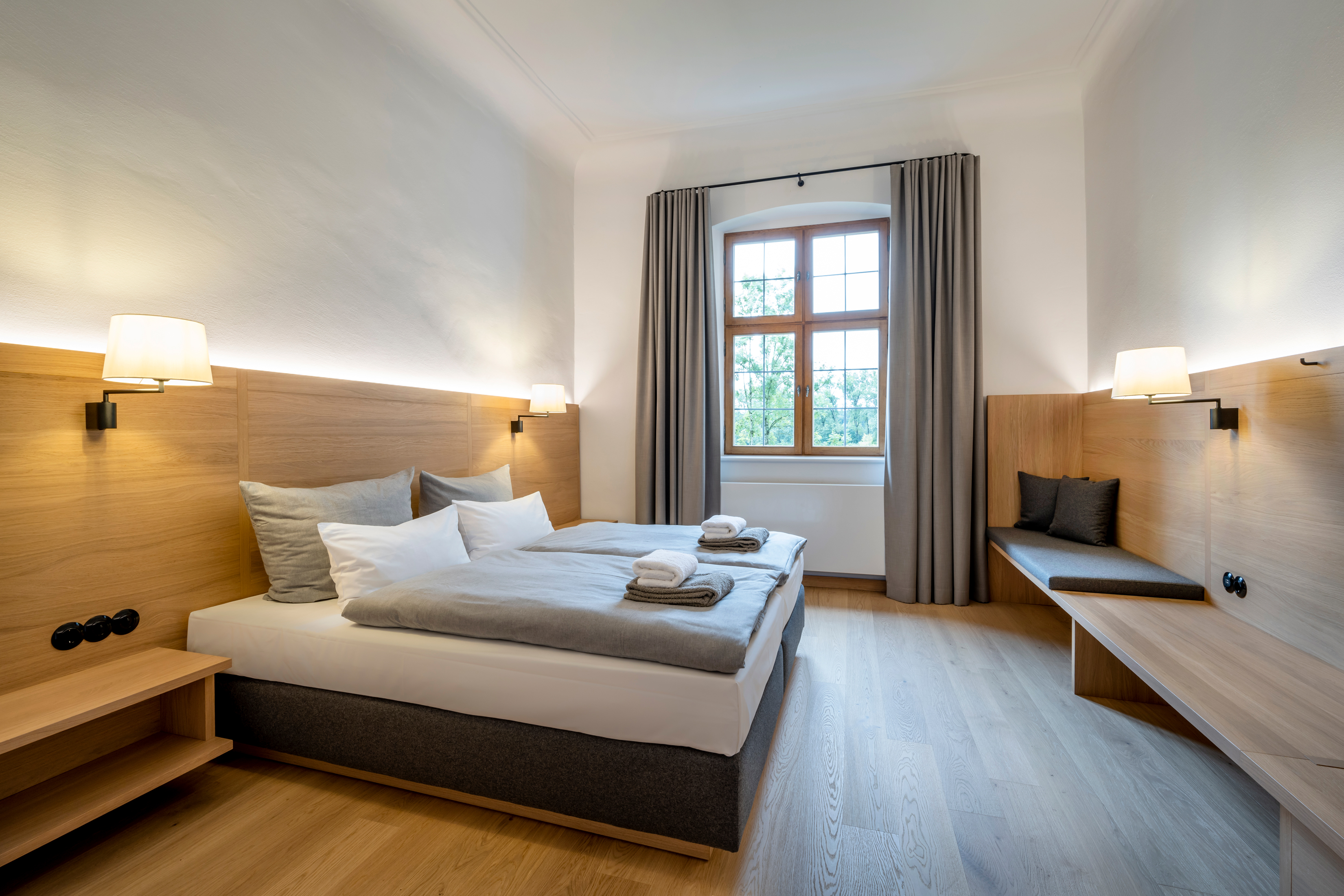 Blick in ein Doppelzimmer mit Holzboden, Beleuchtung und Doppelbett