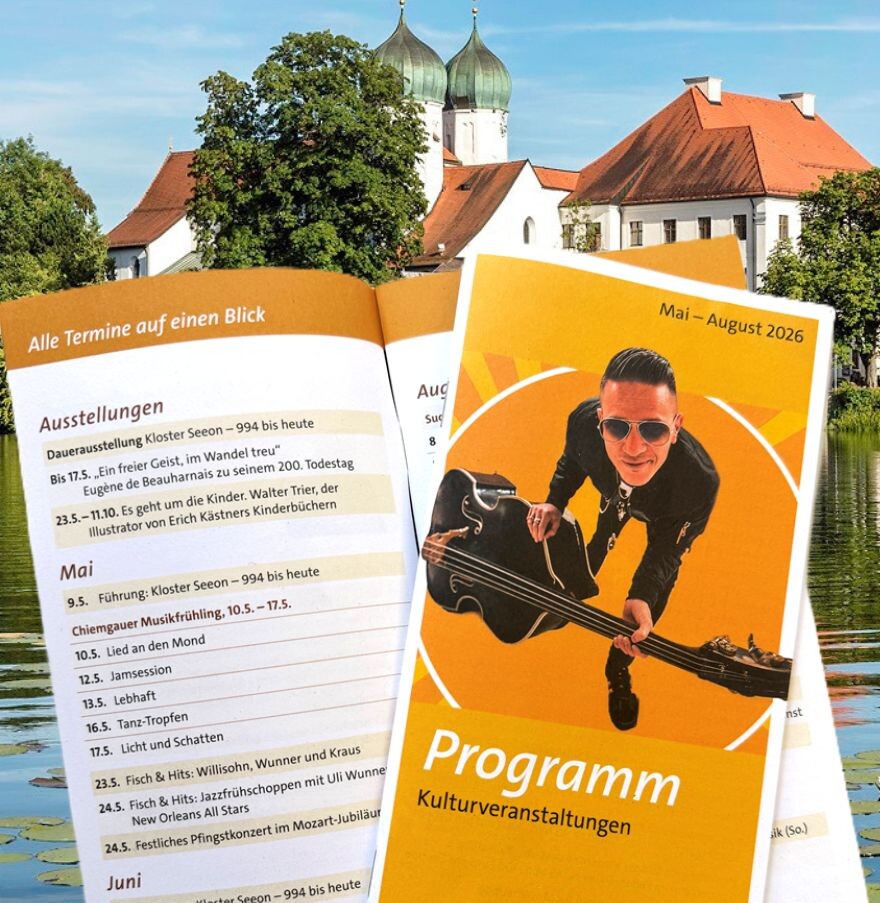 Programmhefte mit Illustration einer Person auf dem Cover liegen auf einer Wiese vor einem hellen Geb&auml;ude mit mehreren Fenstern und einer Sonnenuhr