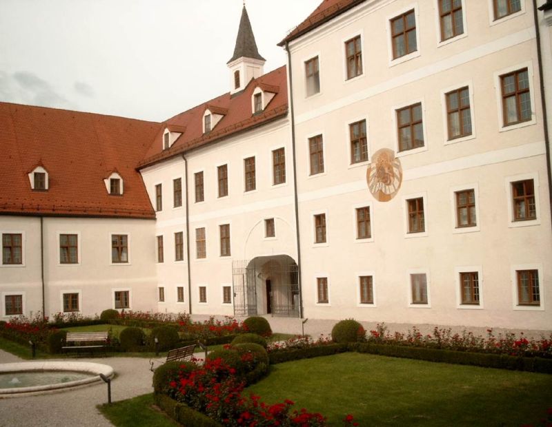 Blick in den Innenhof von Kloster Seeon, die Fassaden sind renoviert und frisch gestrichen, im Vordergrund bl&uuml;hende Rabatten