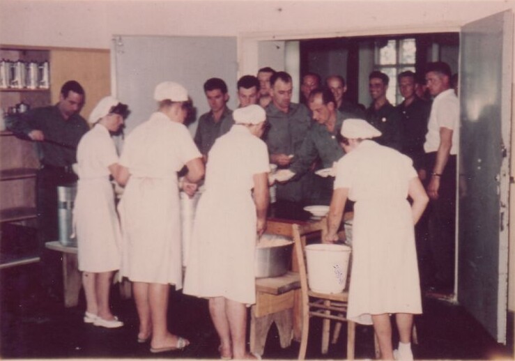 Im Vordergrund wei&szlig; gekleidete K&ouml;chinnen vor gro&szlig;en T&ouml;pfen, im Hintergrund Schlange stehende Polizeisch&uuml;ler