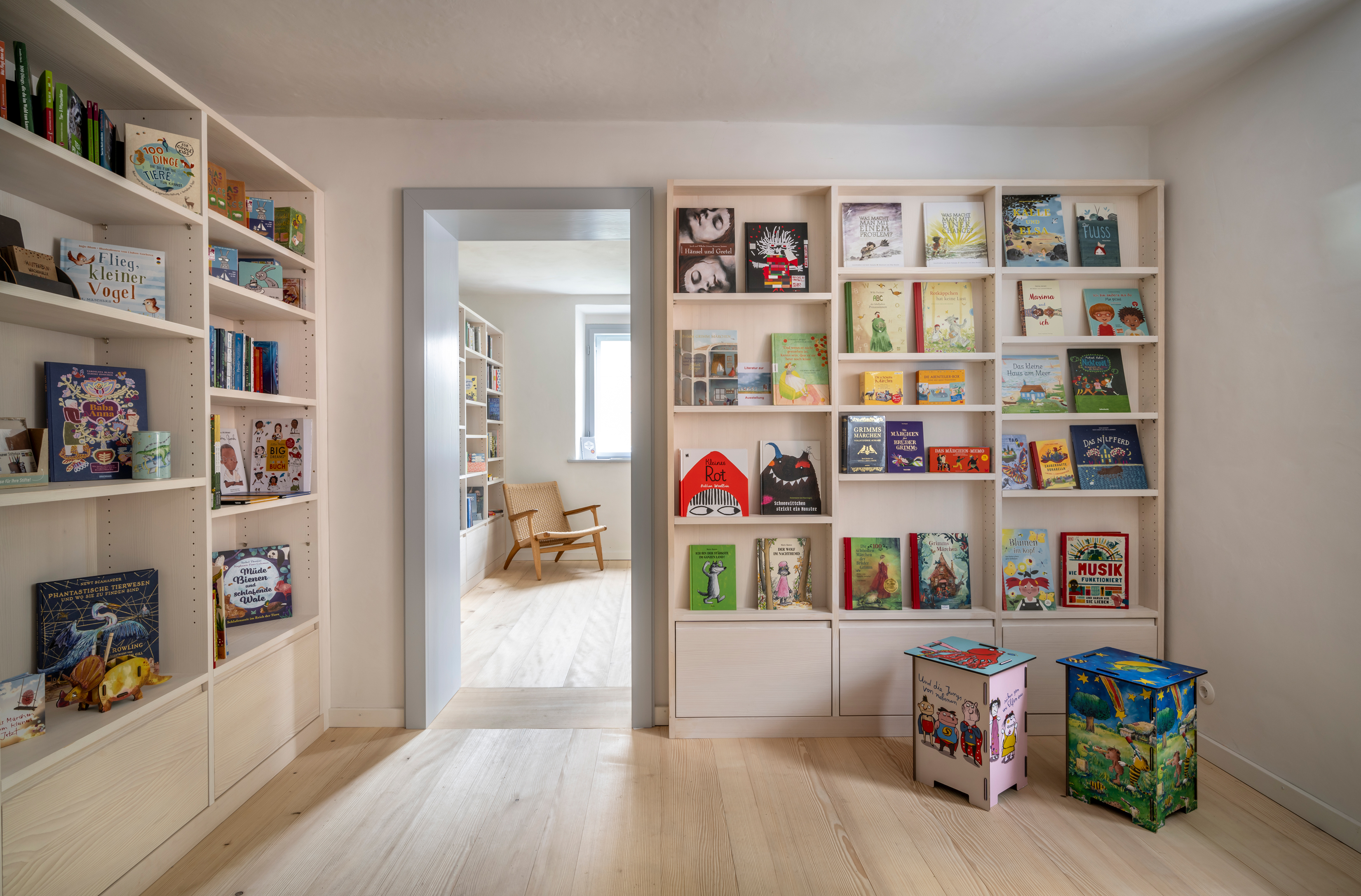 Blick in die helle Bücherstube im Mesnerhaus mit hell lasierten Holzregalen und bunten Büchern