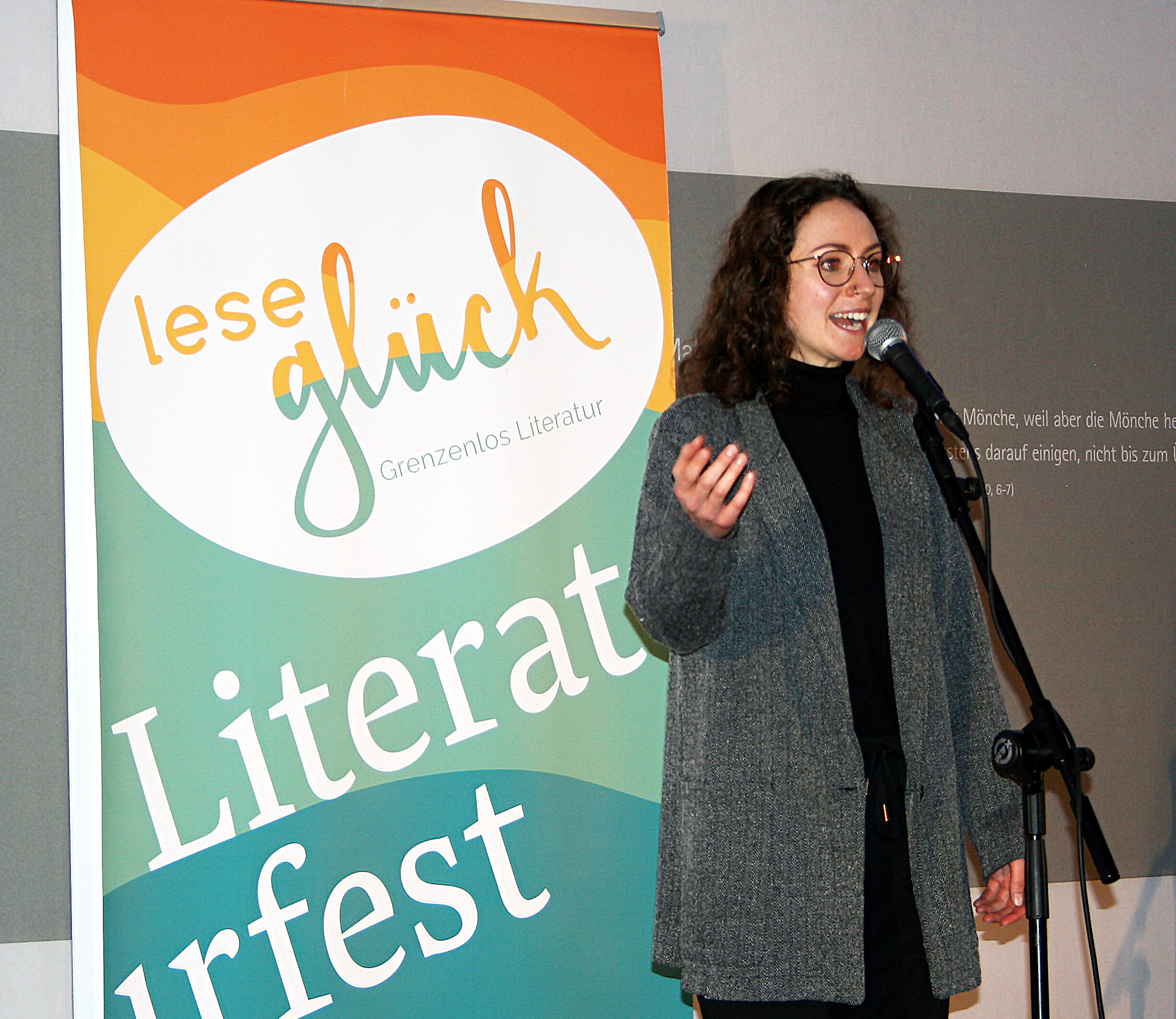 Eine junge Frau steht vor einem Plakat mit der Aufschrift: Leseglück, grenzenlos Literatur, Literaturfest. Sie spricht in ein Mikrofon