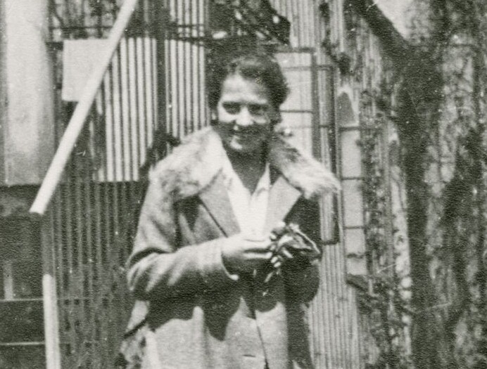 Die schwarz-wei&szlig;-Fotografie zeigt eine junge Frau mit Kost&uuml;m und Mantel gekleidet, l&auml;chelnd vor einer Au&szlig;entreppe von Schloss Seeon im Jahr 2927