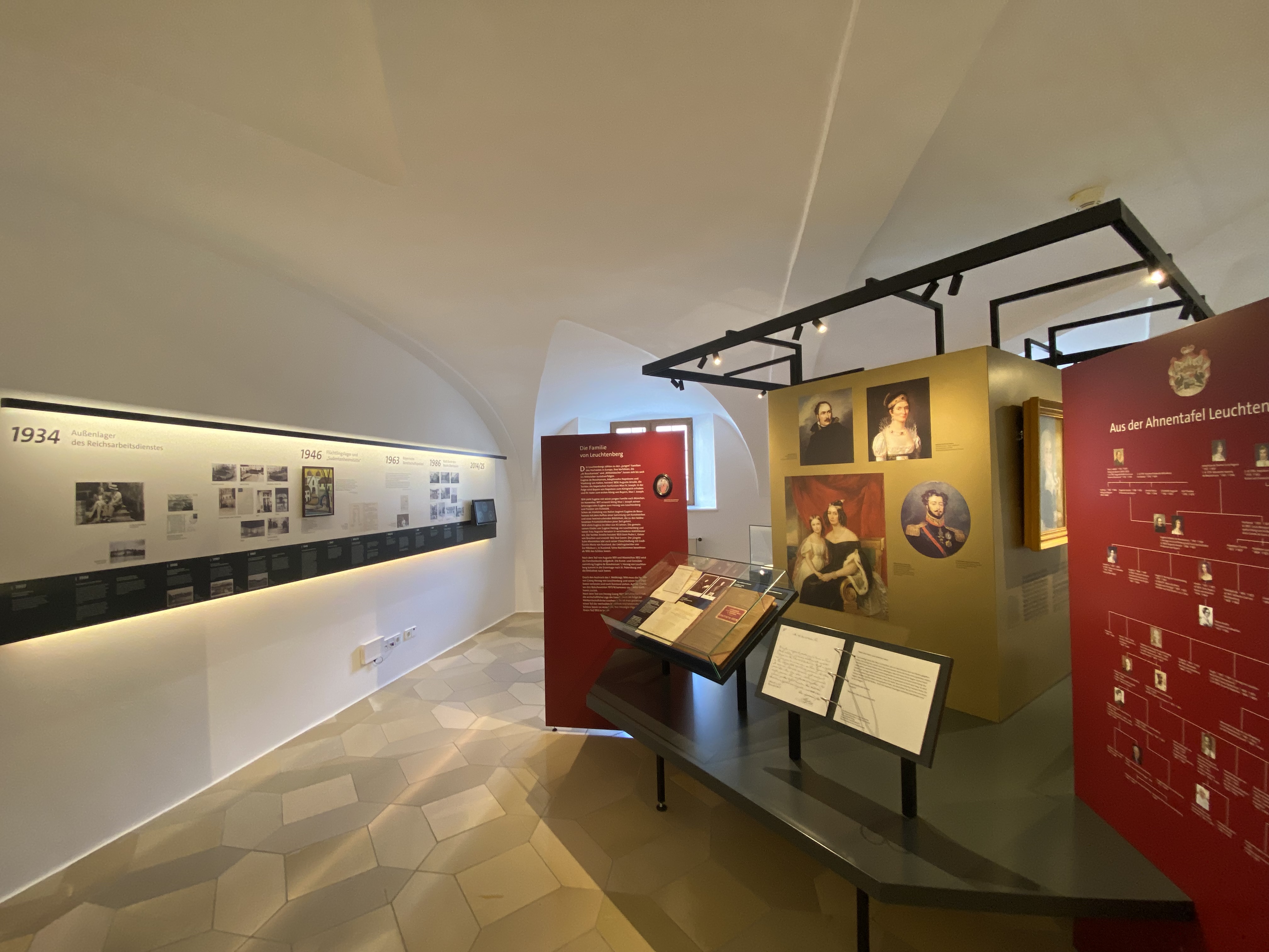 Ausstellung mit beleuchteter Zeitstrahlwand, mehreren Informationstafeln und Portr&auml;tbildern in einem Raum mit gew&ouml;lbter Decke