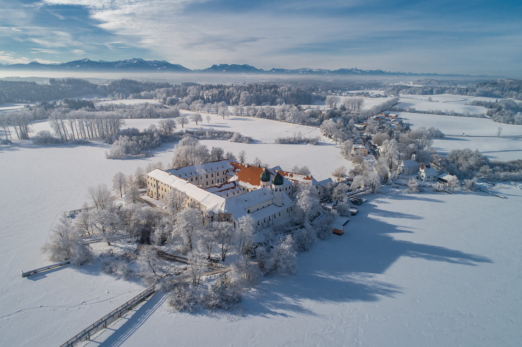 Luftaufnahme vom schneebedeckten Kloster Seeon inmitten des zugefrorenen Sees