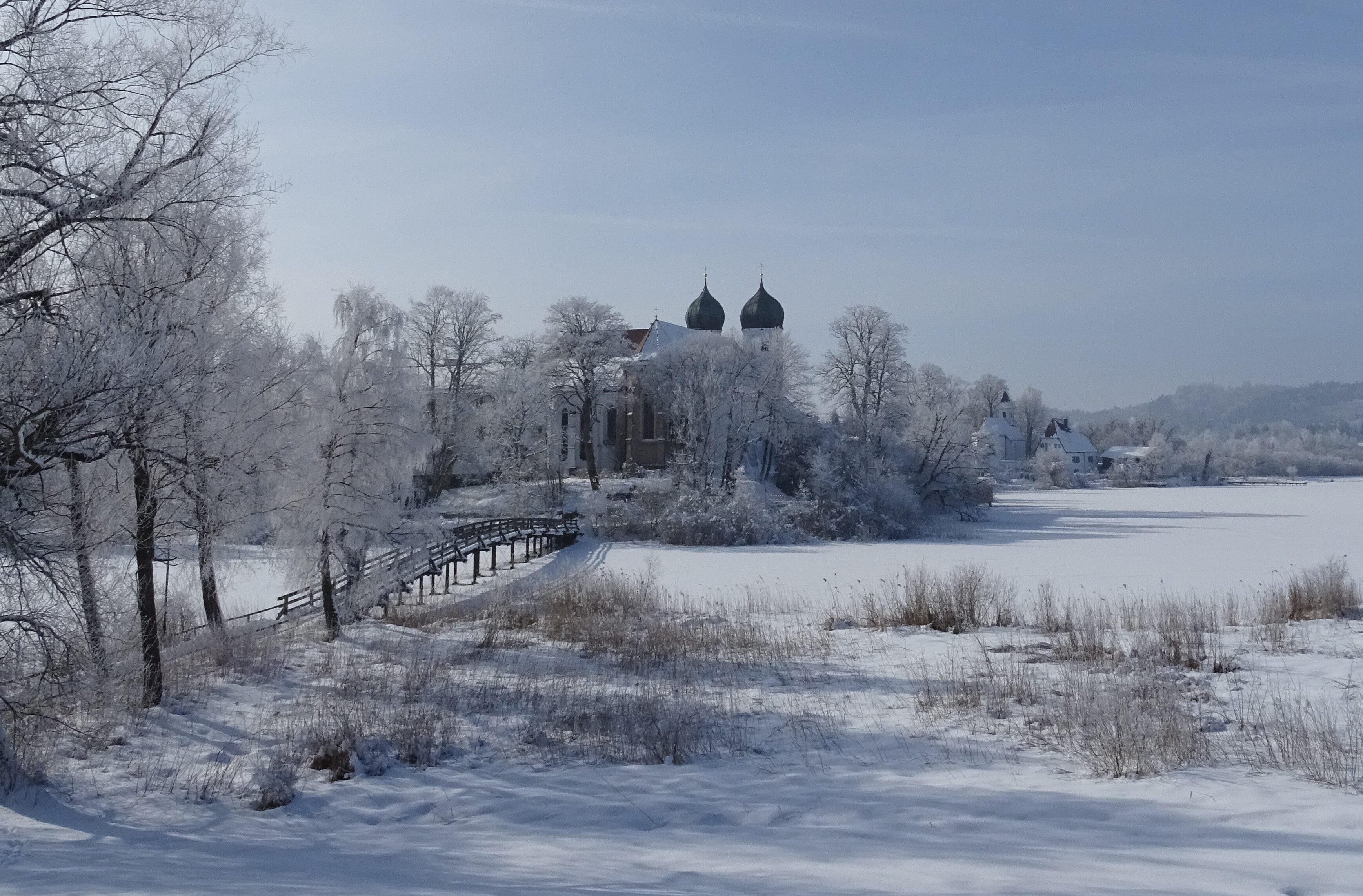 Ansicht von Kloster Seeon von Osten: Brücke über den See, im Hintergrund Zwiebeltürme, verschneite Landschaft