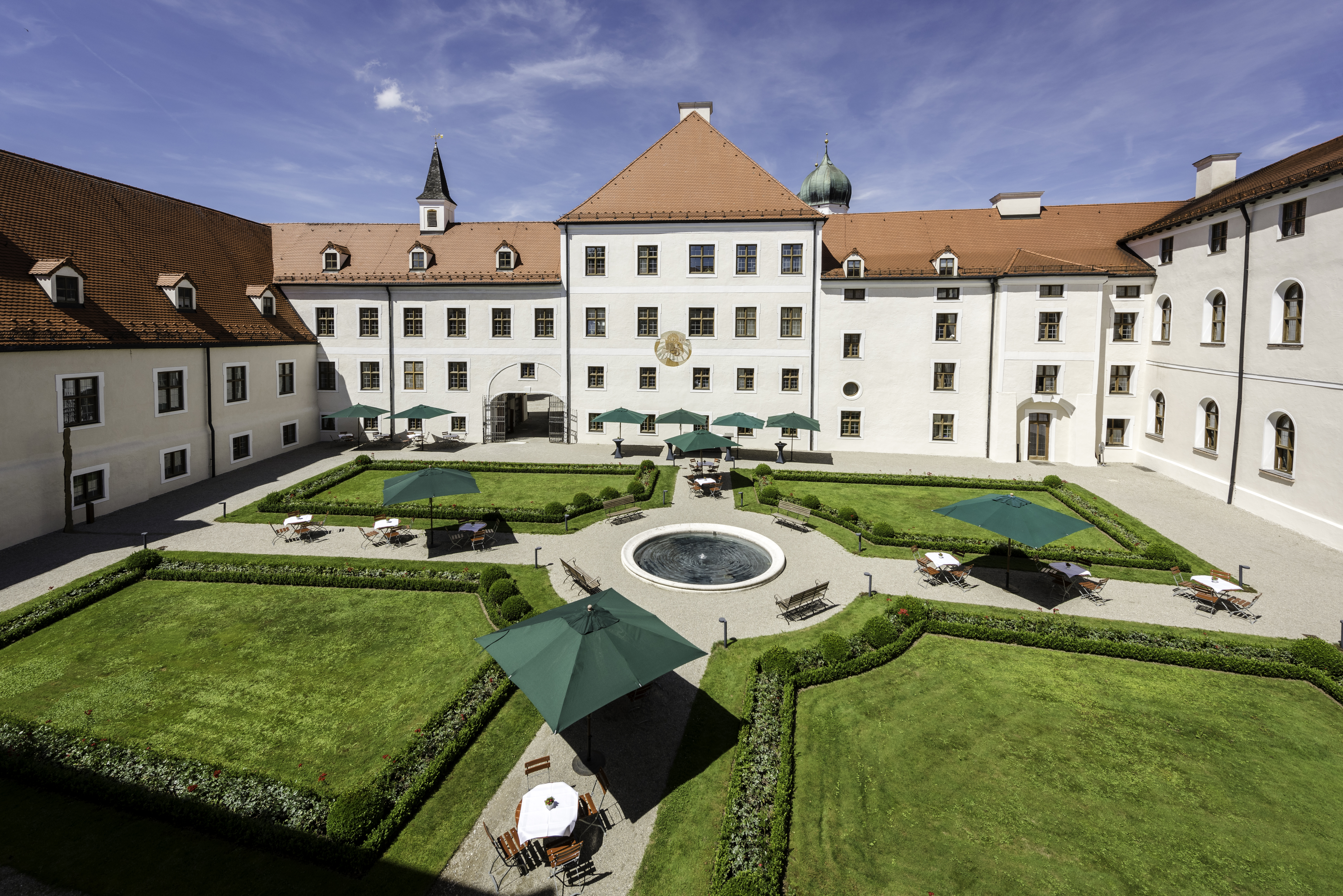 Blick von oben auf den mit Rasenflächen und einem Brunnen geometrisch angeordneten Innenhof von Kloster Seeon