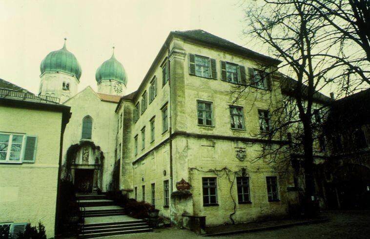 Blick auf den Kirchenaufgang und den alten Abteistock, die Fassade ist verwittert.