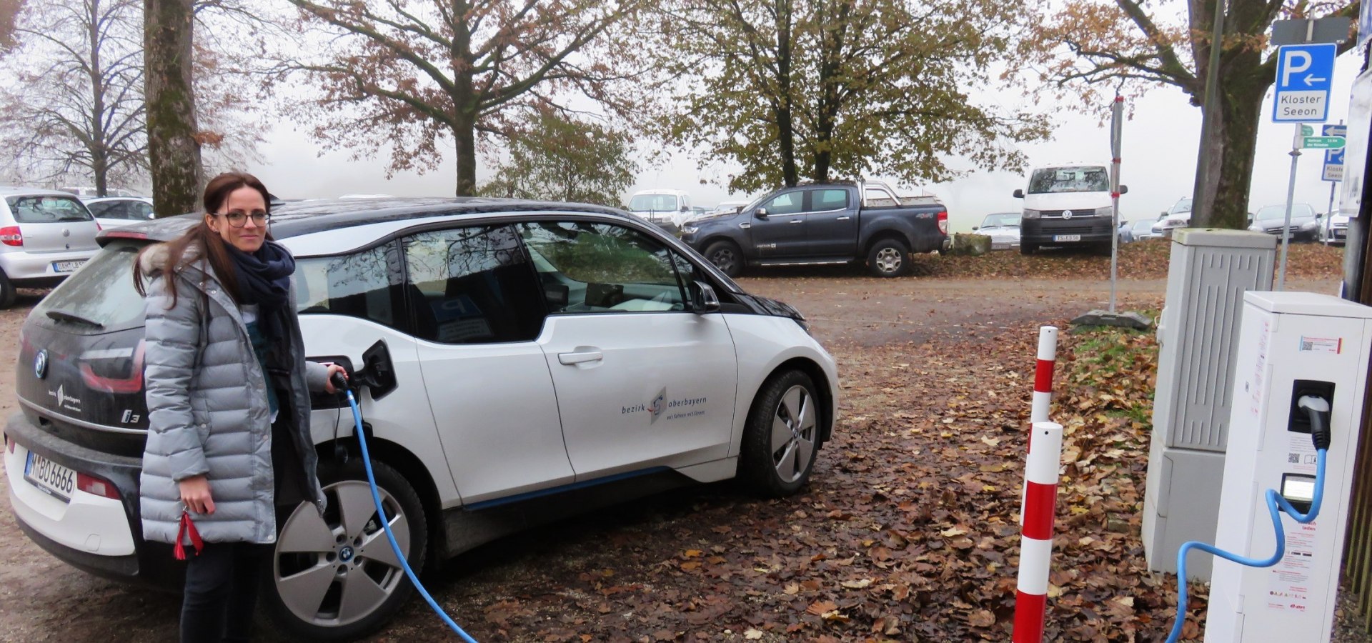 Eine Frau lädt mit einem Kabel ein E-Auto des Bezirks Oberbayern an der Ladestelle von kloster Seeon auf