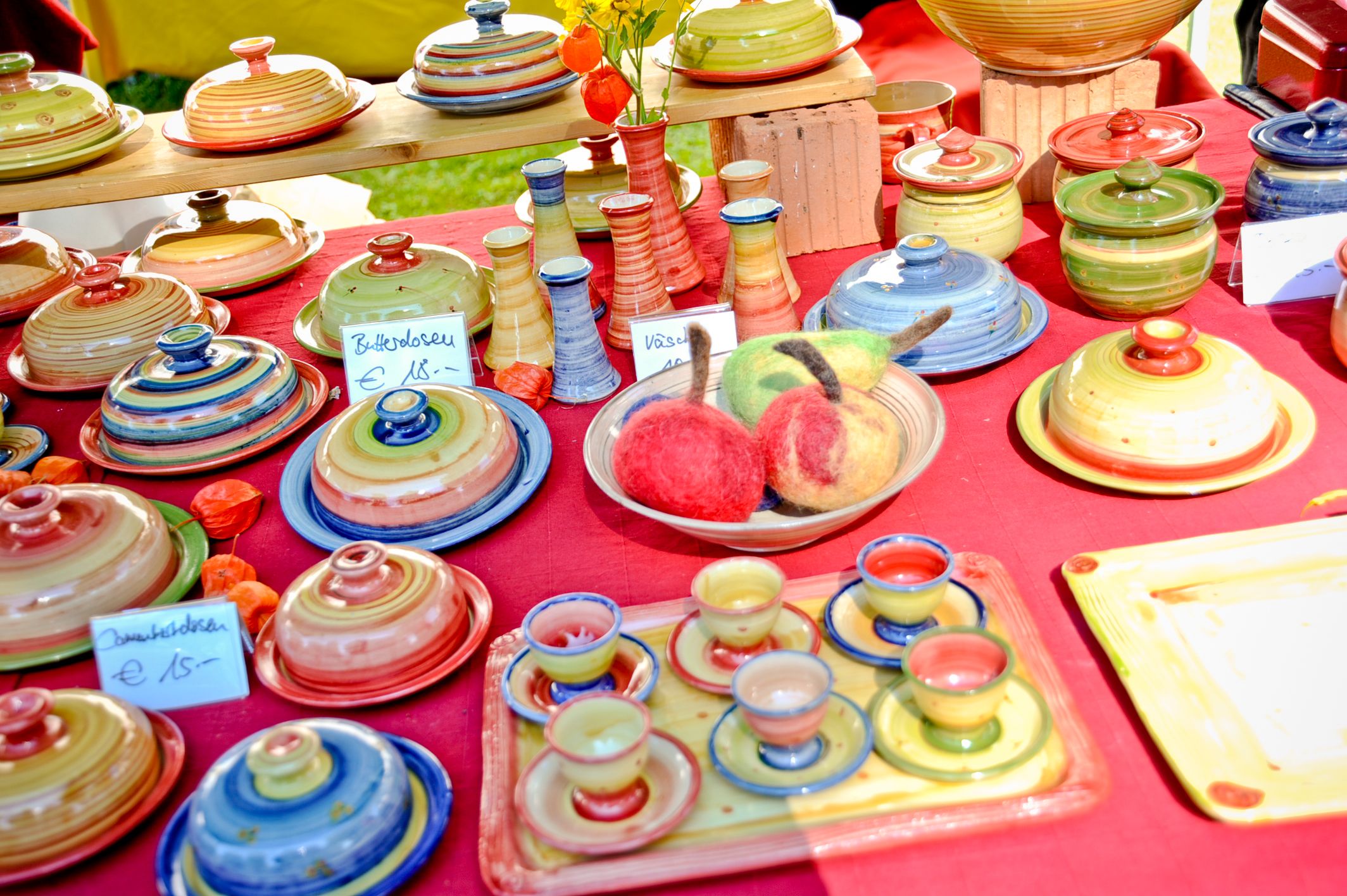 Bunte get&ouml;pferte Keramik wie Butterdosen, Eierbecher, Vasen, Zuckerdosen auf einem Tisch mit rotem Tischtuch beim Kl&ouml;sterlichen Markt in Kloster Seeon