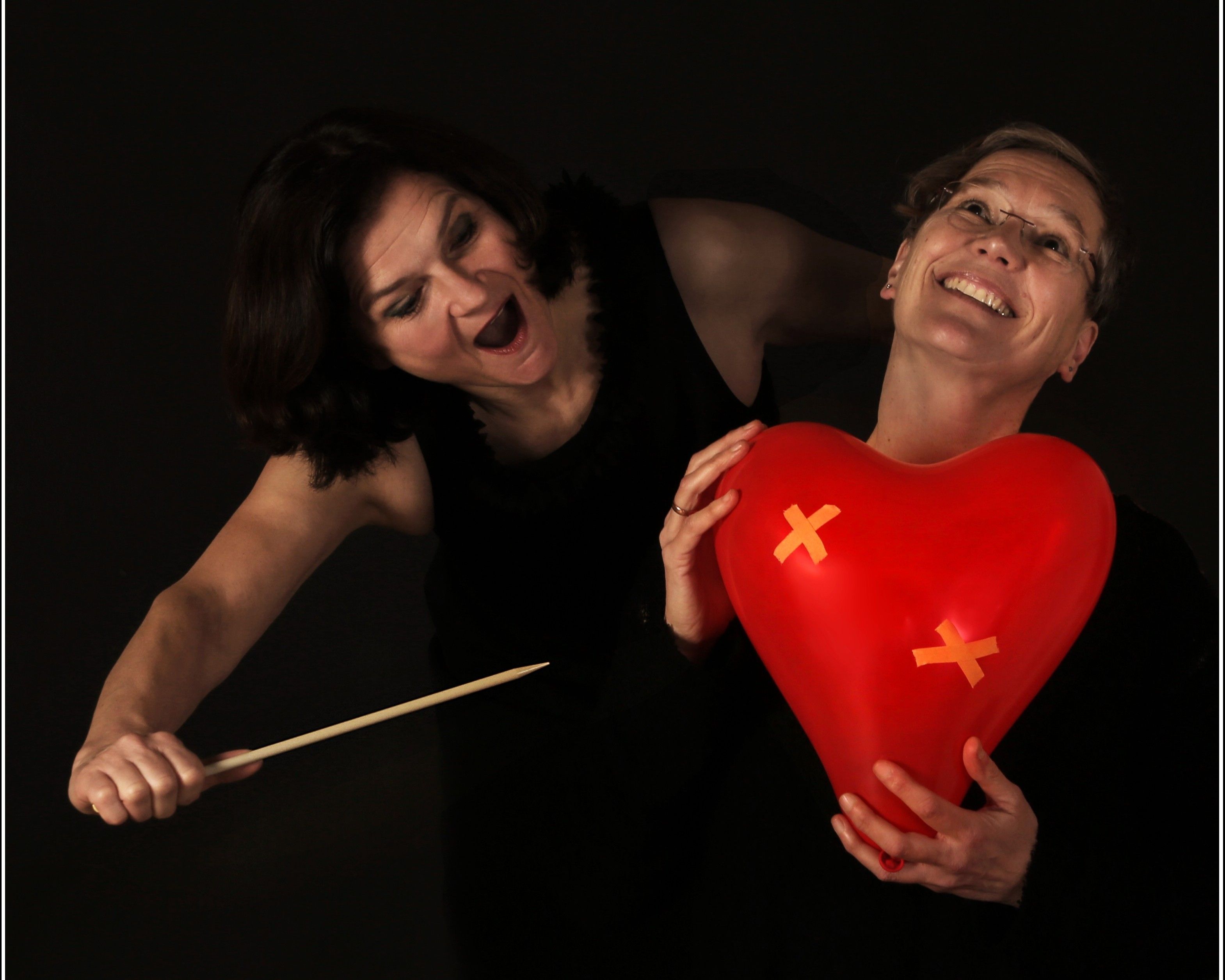 Friederike Duetsch und Maria Bittel mit roten Herz Luftballon und einer gro&szlig;en Nadel in der Hand