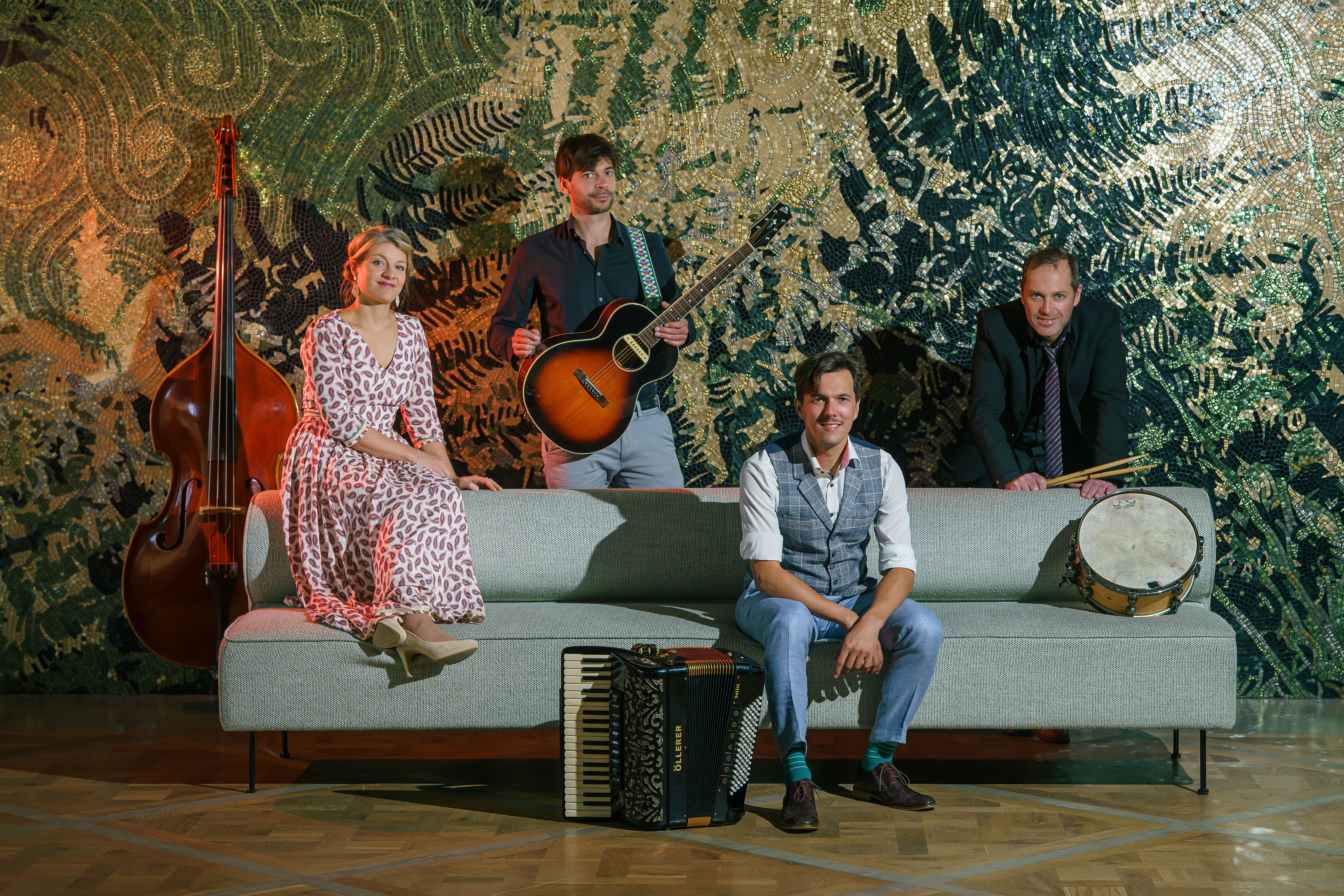 Quartett REIWAS sitzend auf einem grauen Sofa mit Akkordeon, Kontrabass, Gitarre und Trommel 