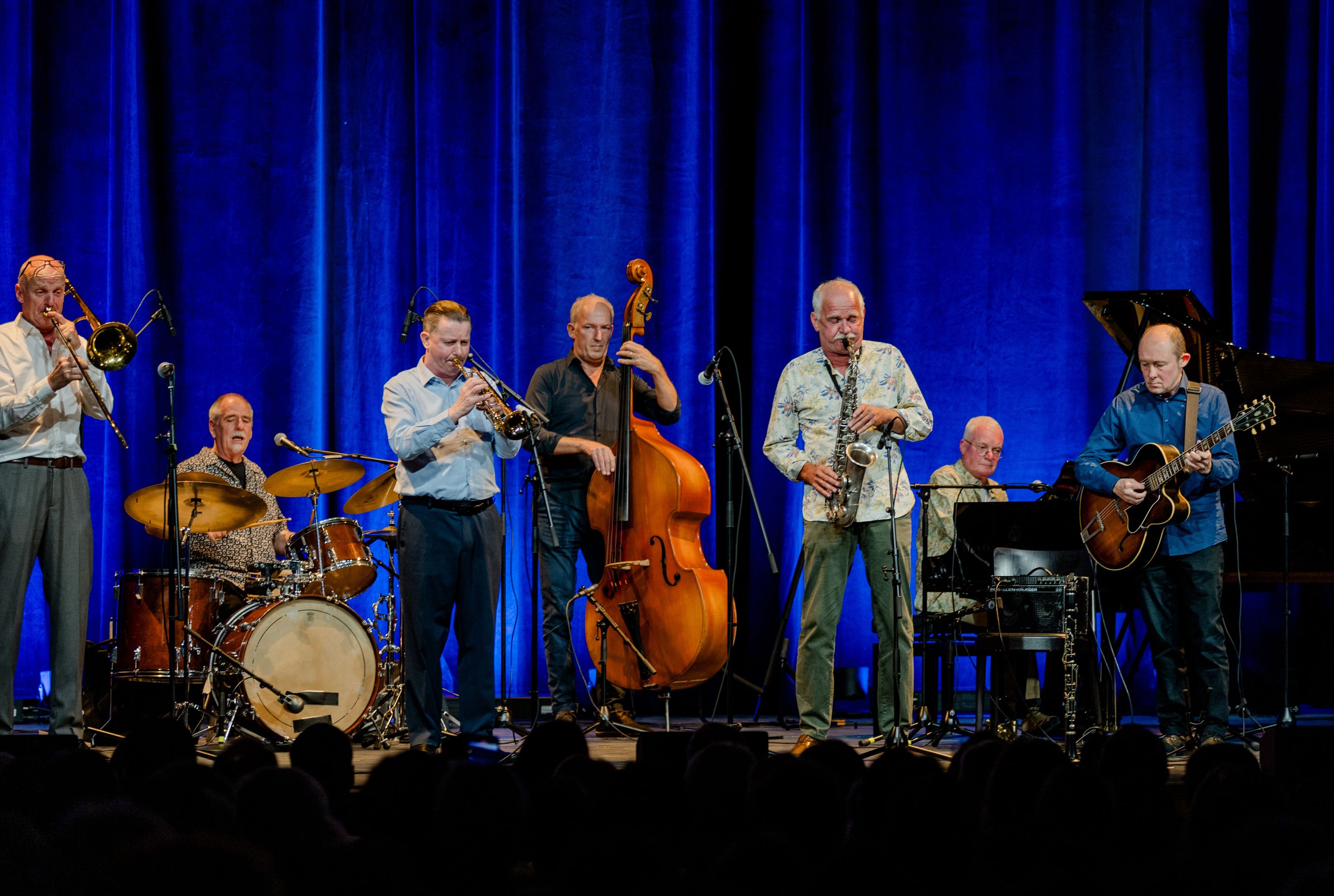 Storyville Shakers und Colin Dason auf einer B&uuml;hne mit blauem Hintergrund und den Instrument Fl&uuml;gel, Posaune, Gitarre, Bass, Schlagzeug und Trompete.
